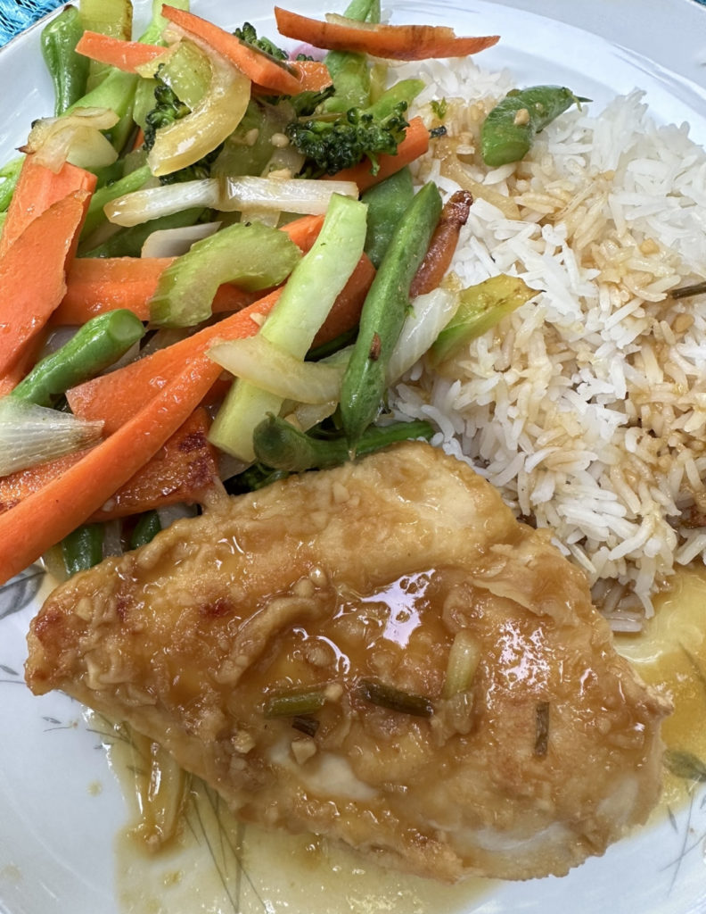 A dinner plate with vegetables, chicken, and rice